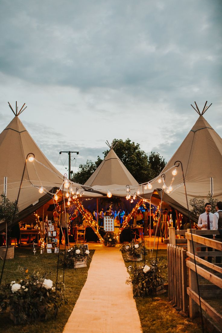 several tents with lights on them are set up in the grass near a path that leads to a wooden fence