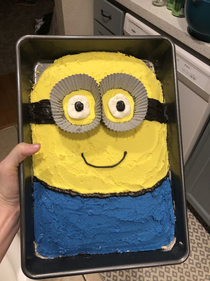 a person holding up a cake shaped like a minion