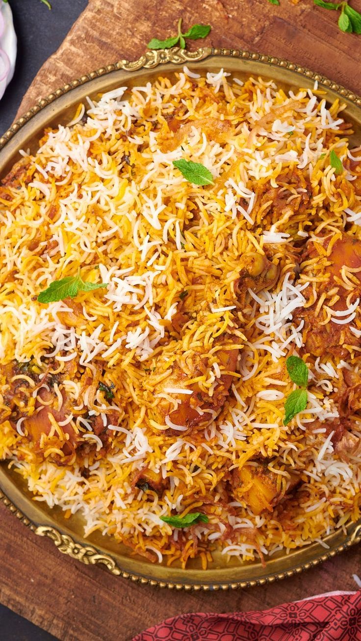 a plate full of rice and meat on top of a wooden board with flowers in the background