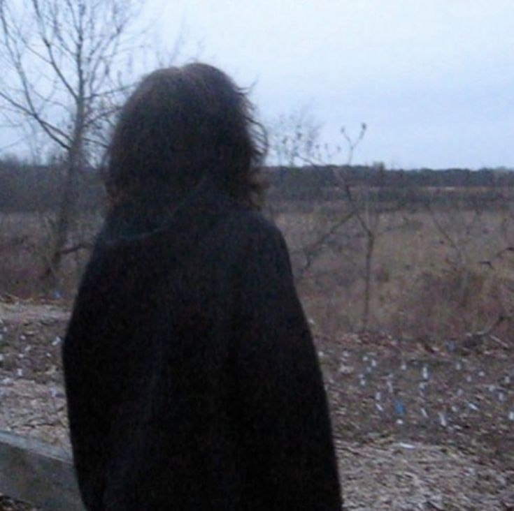 a person standing in front of a bench looking out at the grass and trees behind them