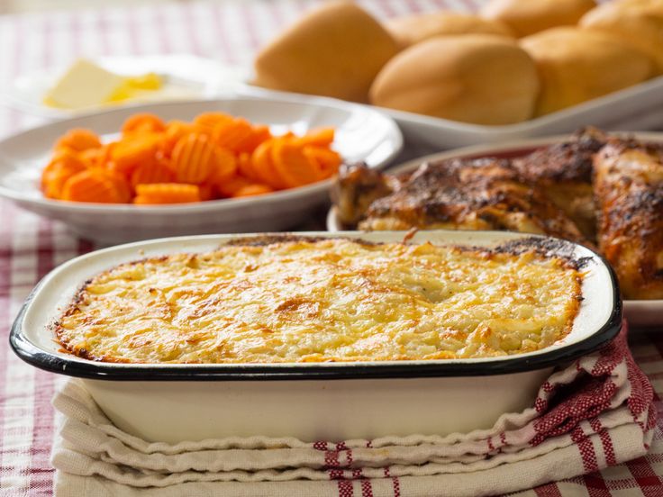 a casserole dish with meat, carrots and bread in the background on a checkered tablecloth