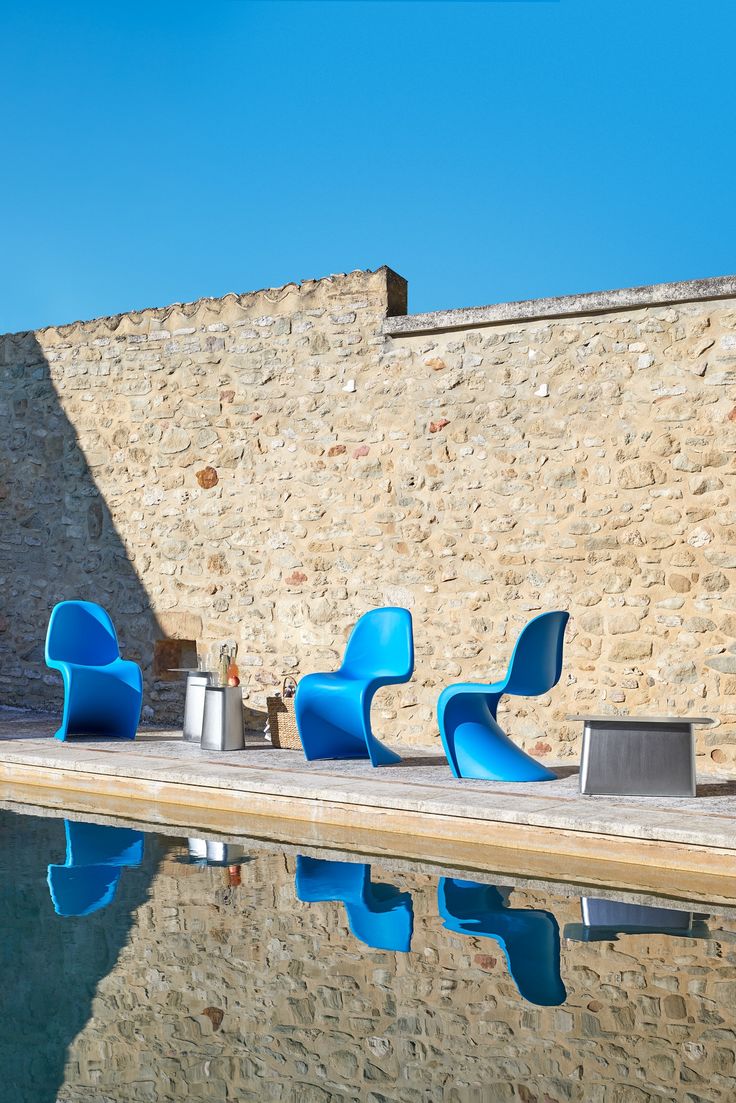 two blue chairs sitting on the side of a pool next to a stone wall and water