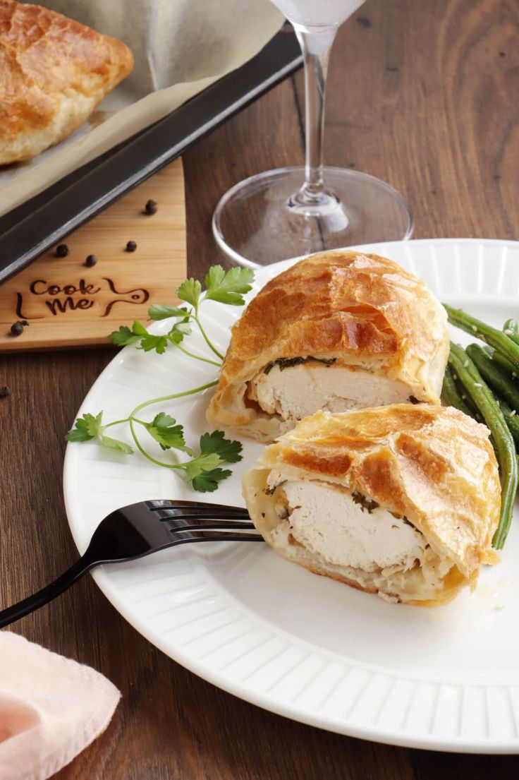 a white plate topped with chicken and green beans next to a glass of wine on a wooden table