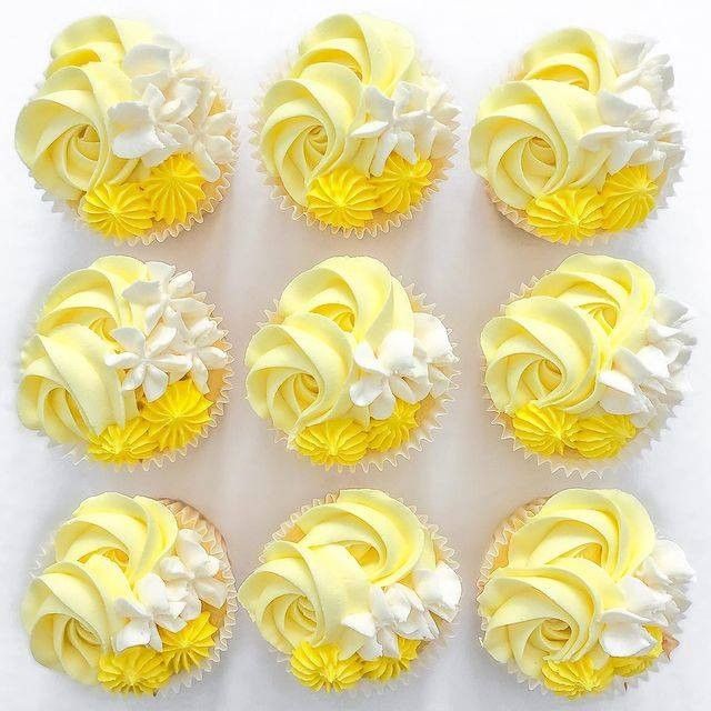 nine cupcakes with yellow frosting and white flowers on them are arranged in rows