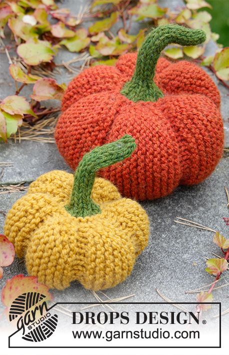 two knitted pumpkins sitting on top of a pile of leaf covered ground next to each other