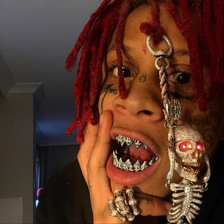 a man with red dreadlocks holding his face to his mouth while wearing skeleton jewelry