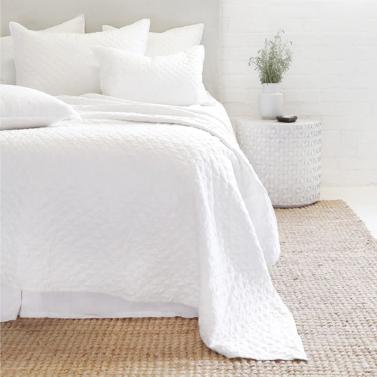 a bed with white linens and pillows in a small room next to a potted plant