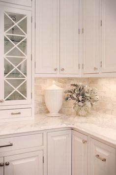 a white kitchen with marble counter tops and cabinets in the corner, along with a vase filled with flowers