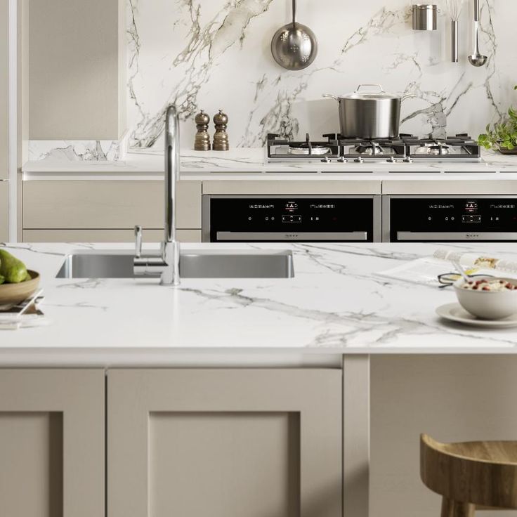 a white kitchen with marble counter tops and stainless steel range hoods over the stove