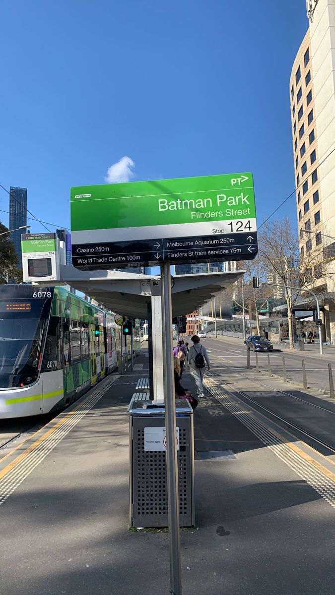 a green and white bus on the street next to a sign that says batman park