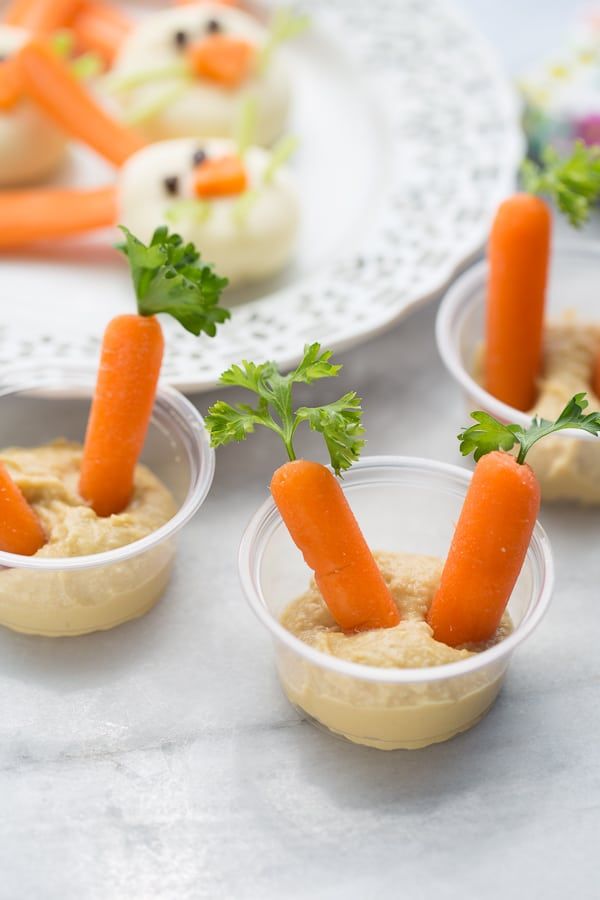 small cups with carrots sticking out of them on a white tablecloth next to other food items