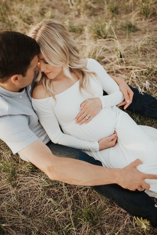 a pregnant couple cuddle while sitting on the ground