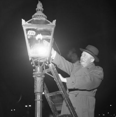 a man in a suit and hat standing next to a street light with his hand on the lamp