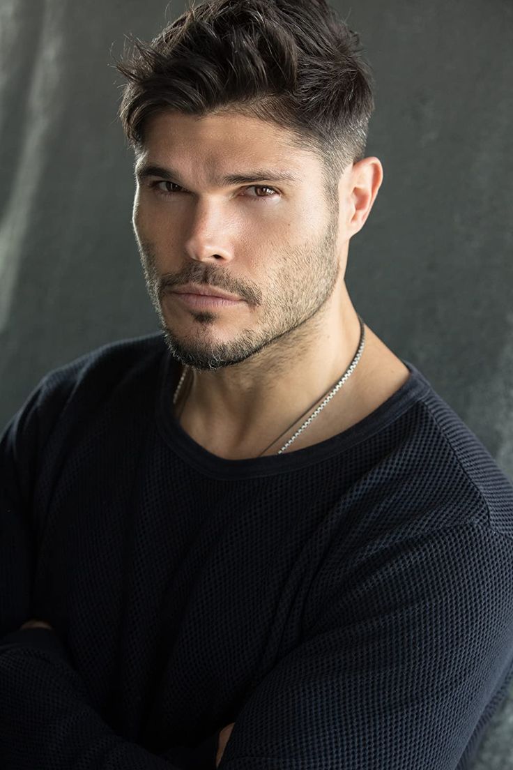 a young man with his arms crossed posing for a photo in front of a gray background