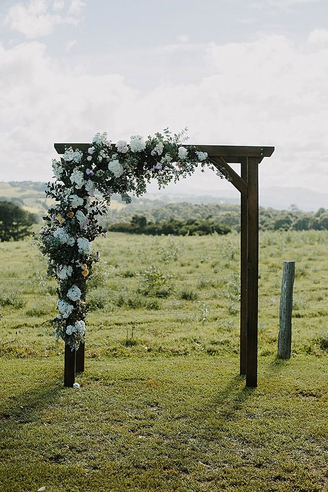 a wooden arch decorated with flowers and greenery in the middle of an open field