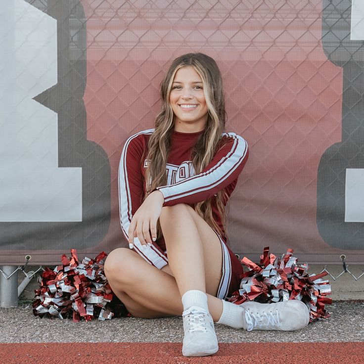 a cheerleader sitting on the ground with her pom poms around her ankles