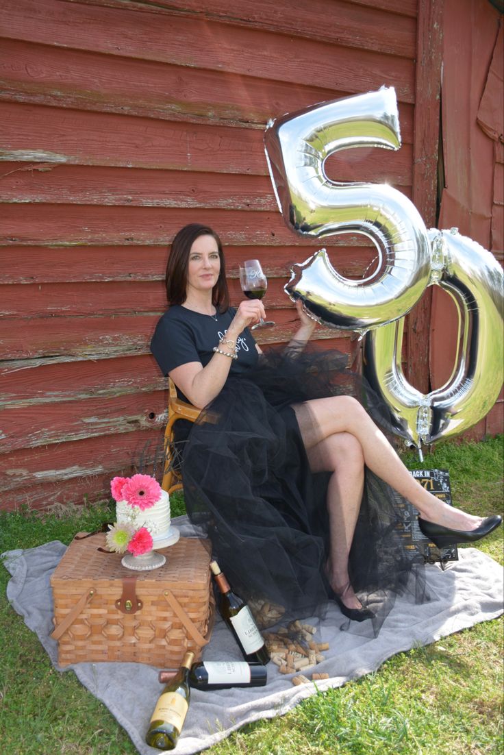 a woman sitting on a blanket holding a glass of wine in front of the number 55 balloon