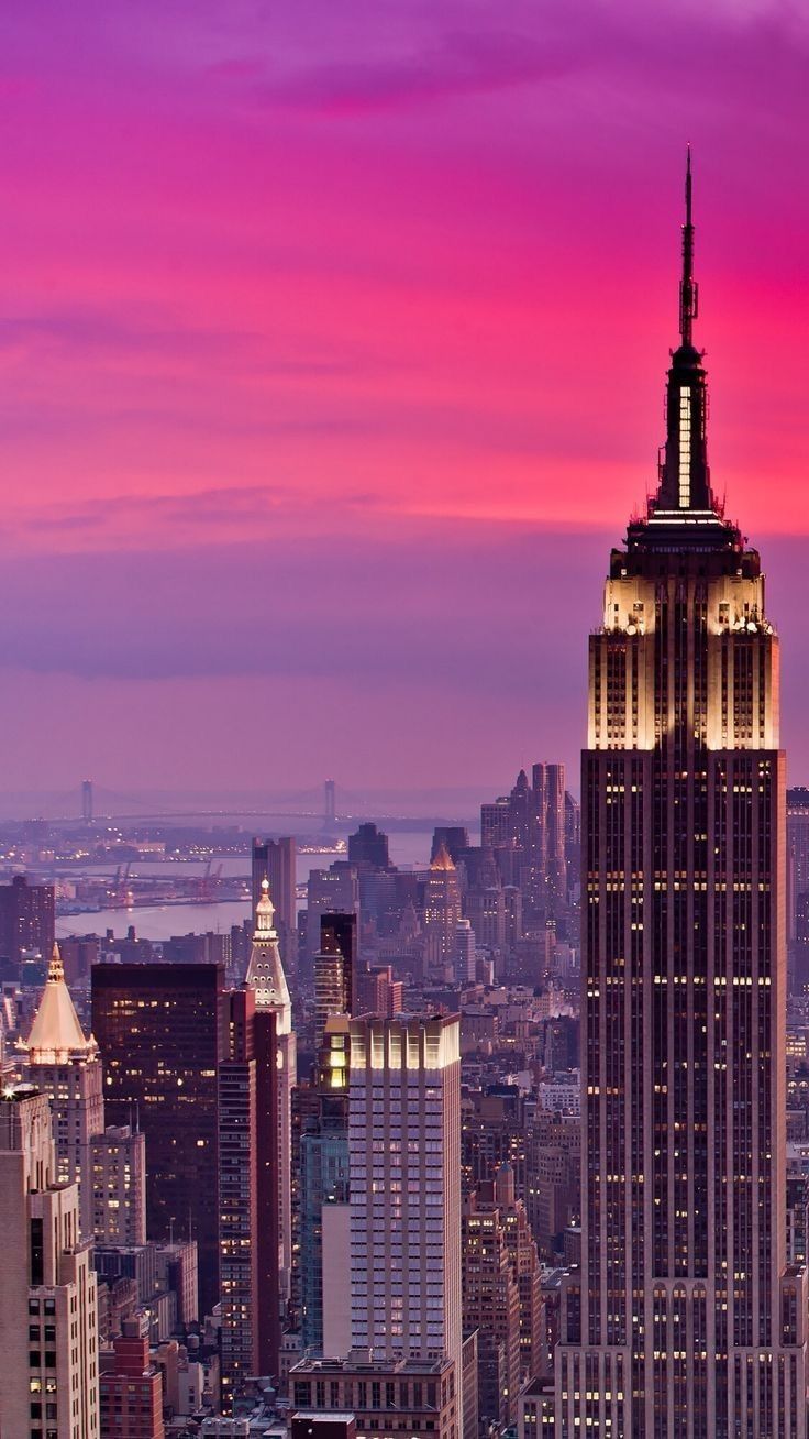 the empire building is lit up at night in new york city, with pink and purple skies