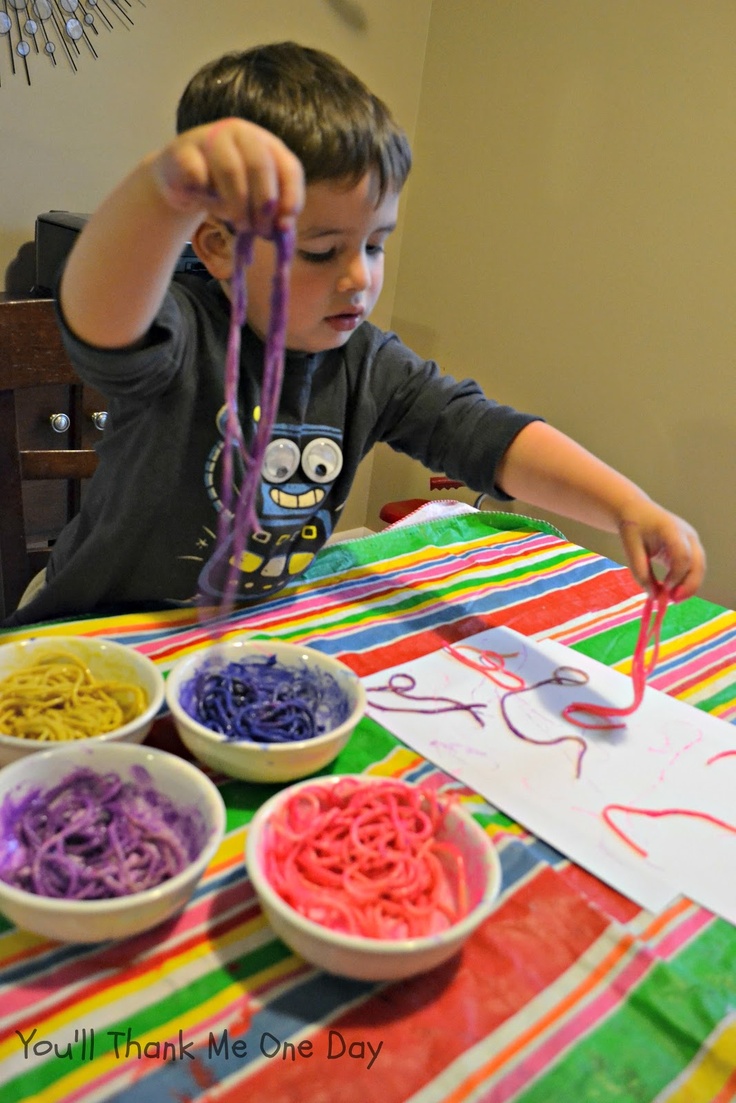 a young boy sitting at a table with bowls of noodles and scissors in front of him