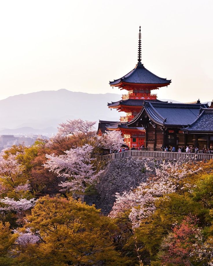 a tall building sitting on top of a lush green hillside next to trees with white flowers