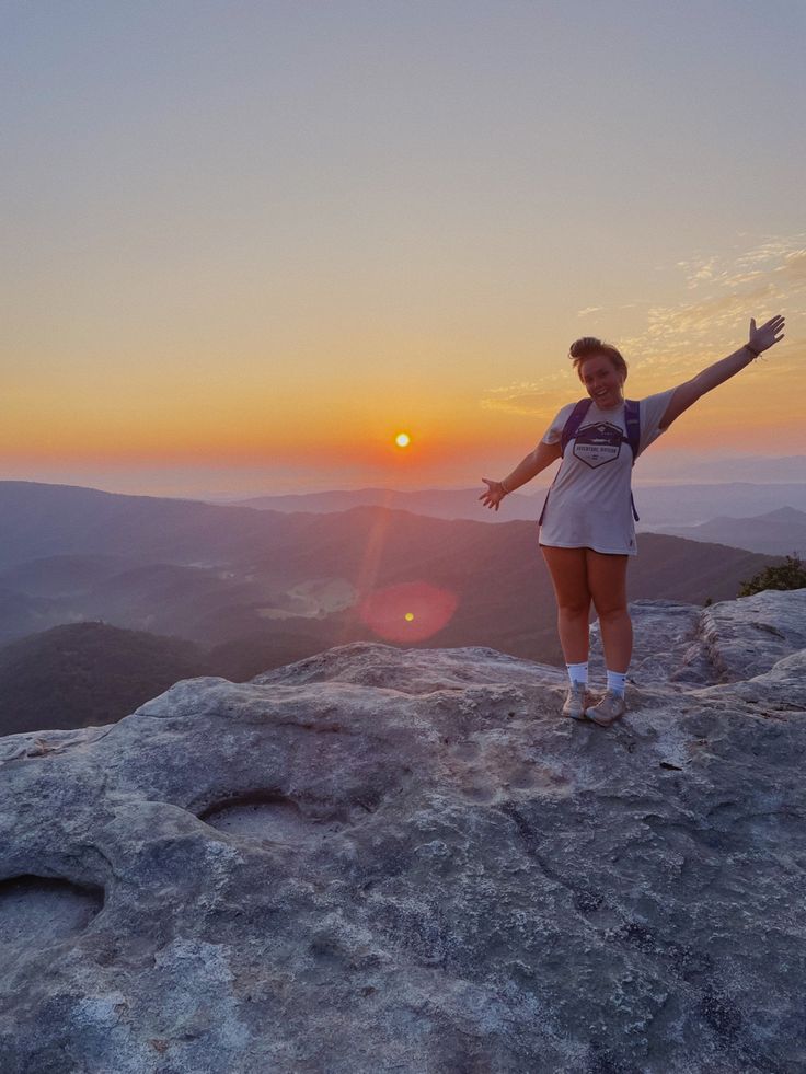 a woman standing on top of a rock with her arms outstretched in front of the sun