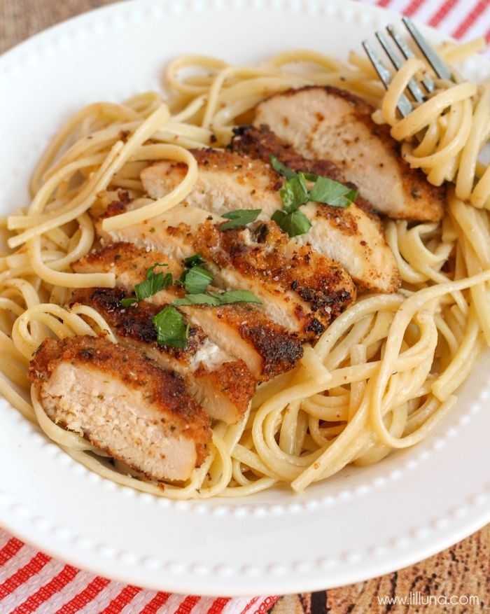 a white plate topped with pasta and meat covered in parmesan cheese, garnished with fresh green leaves