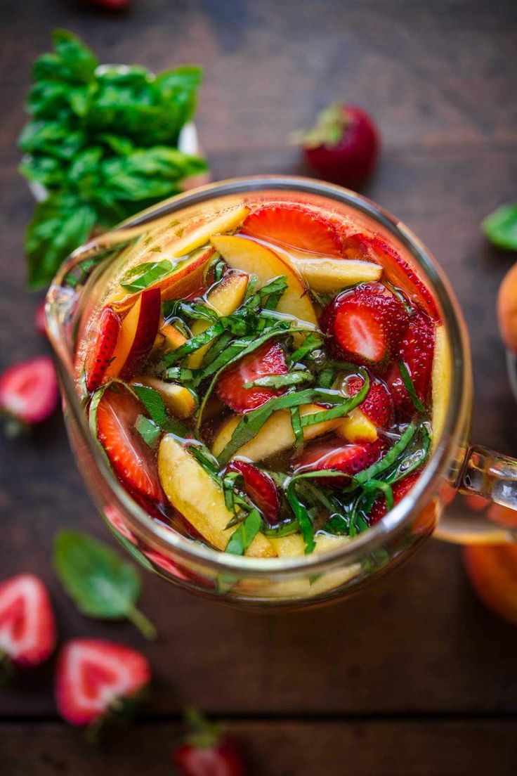 a pitcher filled with fruit and vegetables on top of a wooden table