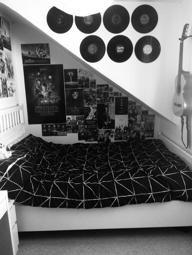 black and white photograph of a bed with many records on the wall above it next to a guitar