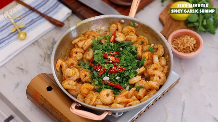 a pan filled with shrimp and vegetables on top of a counter next to a wooden spatula