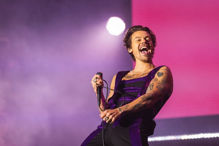 a man with tattoos on his arm holding a microphone and singing in front of a crowd