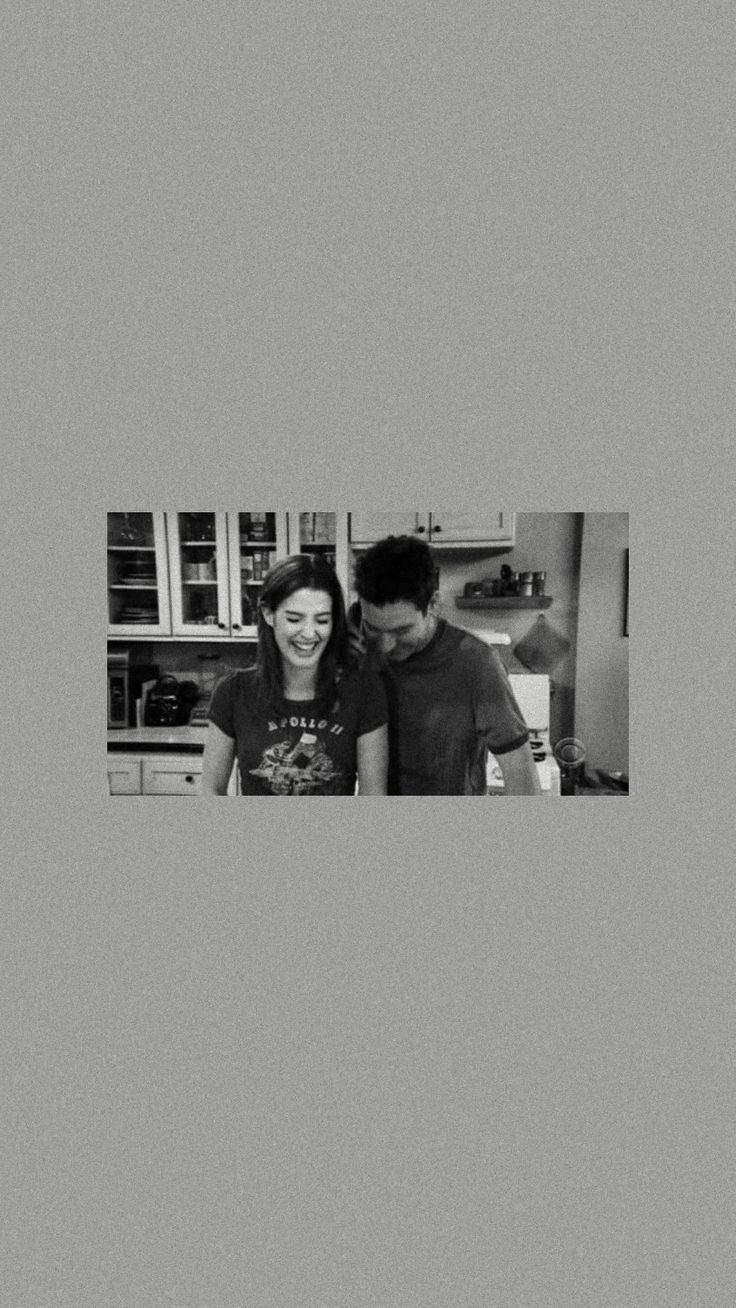 black and white photograph of two people in the kitchen looking at something on the counter