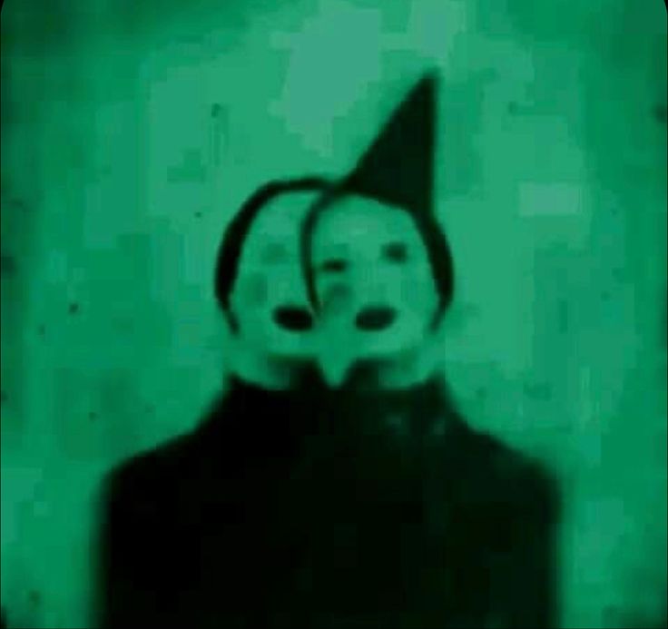 a person wearing a clown mask and holding a cell phone up to their face in front of a green background