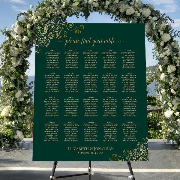 a green and white wedding seating chart with flowers on the top, surrounded by greenery