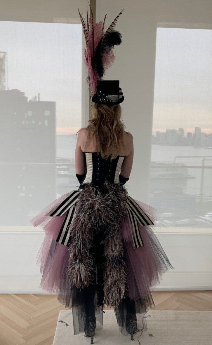 a woman is dressed in black and pink with feathers on her head while standing next to a window