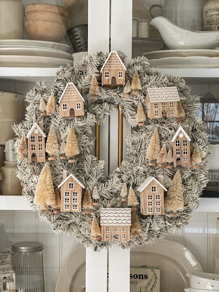 a wreath with houses and trees on it in front of a hutch full of dishes