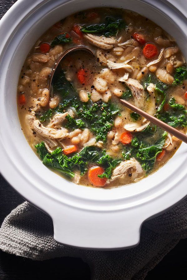 a white bowl filled with chicken and spinach soup on top of a black table