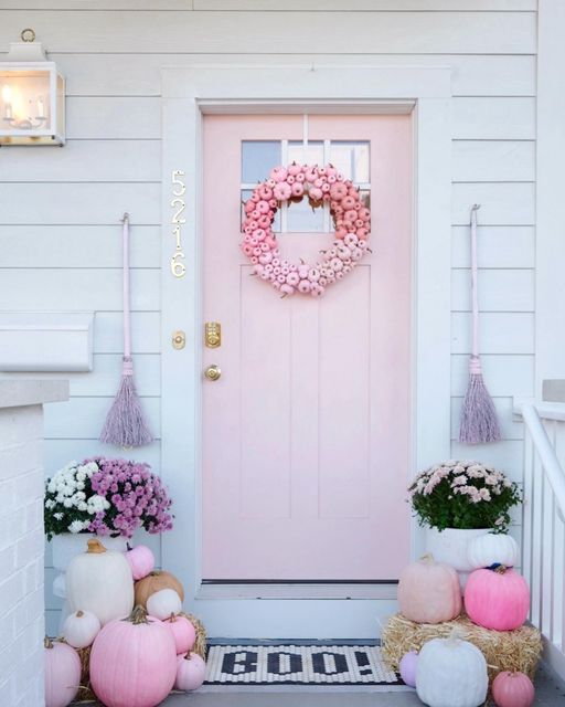 a pink front door decorated with wreaths and fake flowers on the steps to a white house