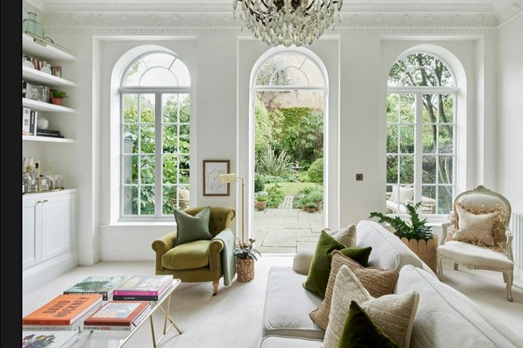 a living room filled with lots of furniture next to two large windows and a chandelier hanging from the ceiling