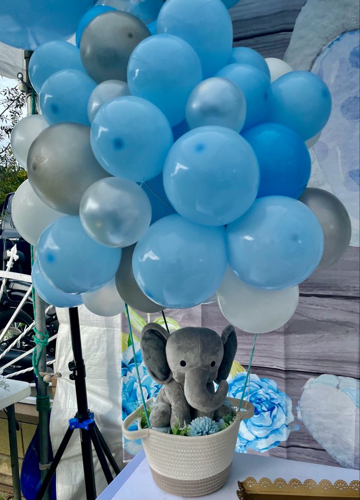 an elephant is sitting in a basket with blue and white balloons attached to its trunk