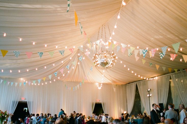 people are gathered in a large tent with lights strung from the ceiling and colorful bunting