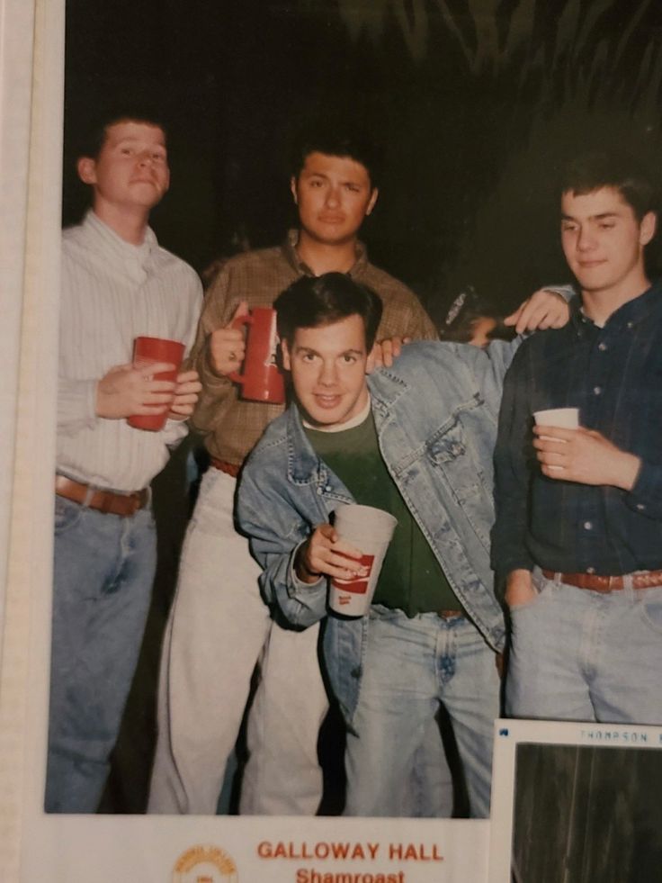 a group of young men standing next to each other holding cups and drinking beverages in their hands