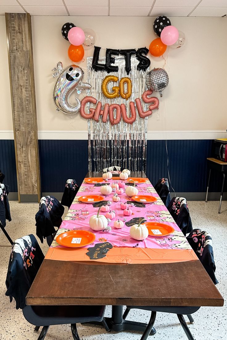 the table is set up for a halloween party with balloons and streamers hanging from the ceiling