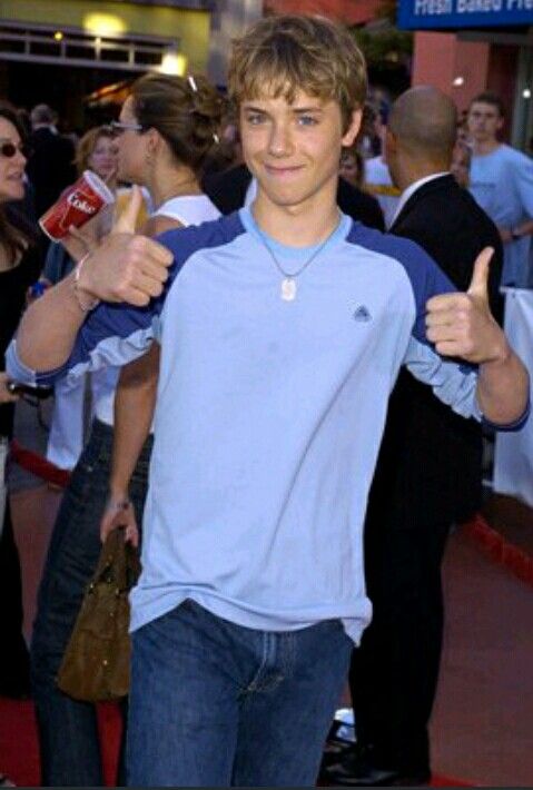 a young man is giving the thumbs up sign at an event with people in the background