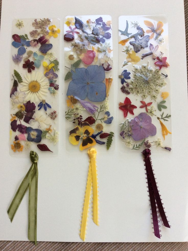 three pieces of paper with flowers and ribbons attached to them on top of a table