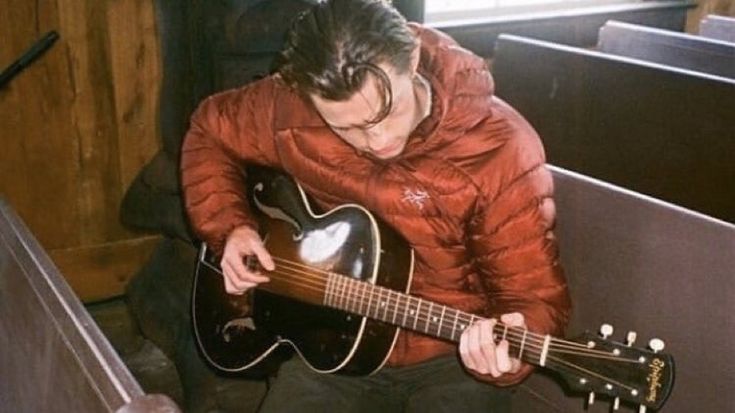 a man sitting down playing an acoustic guitar