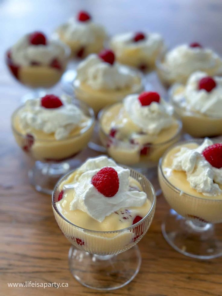 small desserts with whipped cream and raspberries in glass dishes on a wooden table