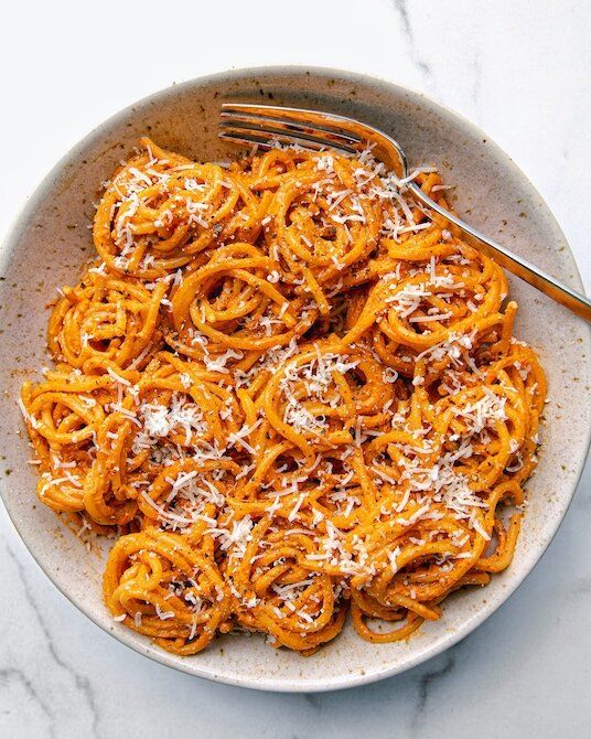 a white bowl filled with pasta and topped with parmesan cheese on a marble table