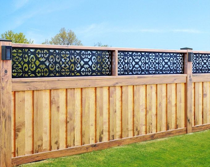 a wooden fence with metal designs on the top and bottom panels, along with green grass