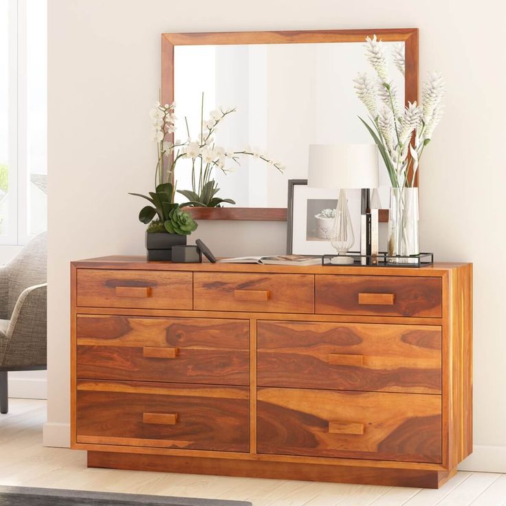 a wooden dresser sitting in front of a mirror and vase with flowers on top of it