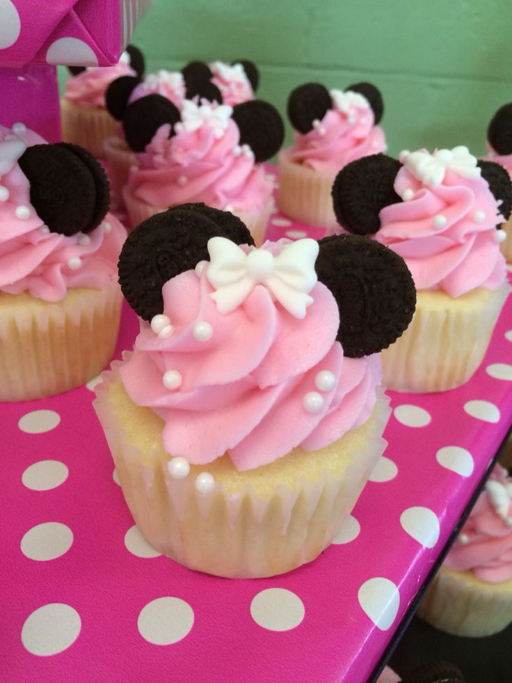 cupcakes with pink frosting and minnie mouse ears on top are sitting on a polka dot table